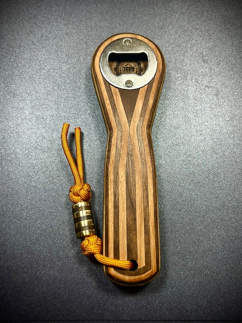 Op de afbeelding: Een houten flessenopener met een metalen dopopener. De opener heeft een gestreept patroon en een bruin koord met een messing kraal.