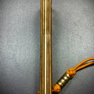 Op de afbeelding: Een houten meshendel met een gelaagd houten ontwerp en een bruin en wit kleurenschema. Een gouden metalen kraal is bevestigd aan een geel koord.