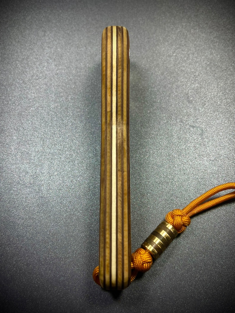 Op de afbeelding: Een houten meshendel met een gelaagd houten ontwerp en een bruin en wit kleurenschema. Een gouden metalen kraal is bevestigd aan een geel koord.