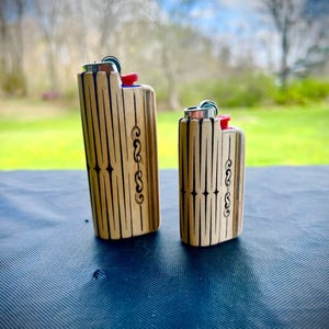 May include: Two wooden lighter cases with a black and white geometric design. The larger case has a blue accent and the smaller case has a red accent.