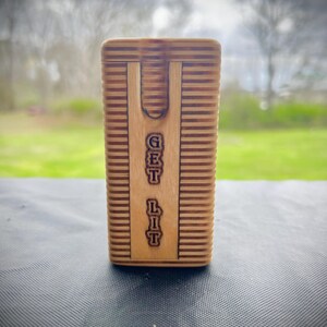 Puede incluir: Una caja de madera con una ranura en la parte superior y las palabras "GET LIT" grabadas en la parte delantera.