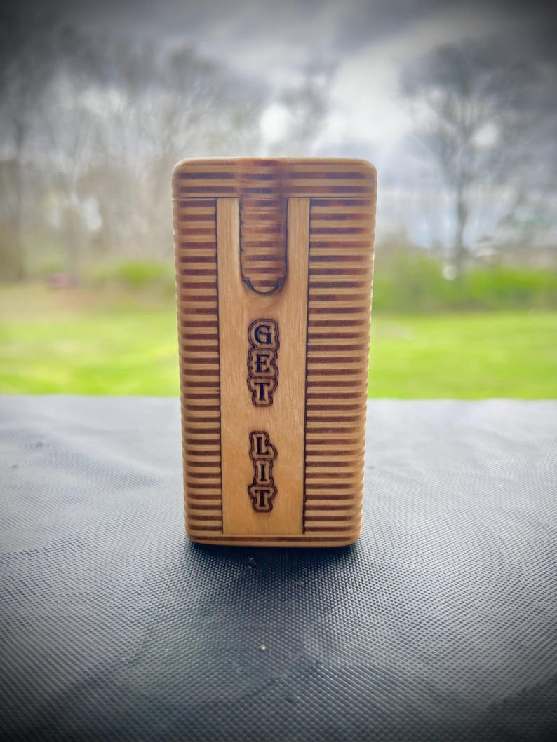 Puede incluir: Una caja de madera con una ranura en la parte superior y las palabras "GET LIT" grabadas en la parte delantera.