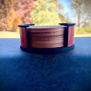 May include: A set of six wooden coasters with a dark brown finish and a red border. The coasters are stacked on top of each other.
