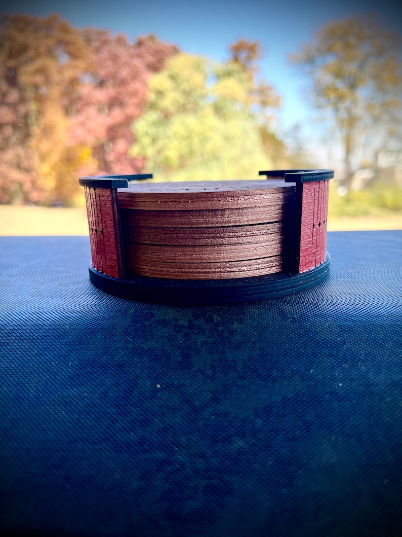 May include: A set of six wooden coasters with a dark brown finish and a red border. The coasters are stacked on top of each other.