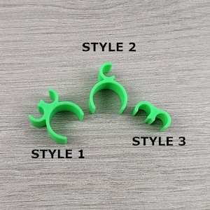 Puede incluir: Tres clips de plástico verde, etiquetados como "STYLE 1", "STYLE 2" y "STYLE 3".