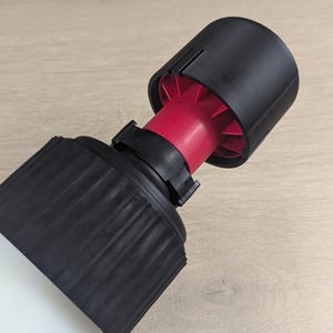 May include: A black and red plastic bottle nozzle with a black cap. The nozzle has a ribbed design and a red ring around the middle.