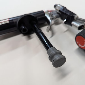 May include: A black and gray spray gun with a gray nozzle. The gun has a black handle and a black trigger. The nozzle has a series of holes in it.