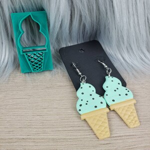 May include: A pair of mint green ice cream cone earrings with black sprinkles. The earrings are made of polymer clay and have silver hooks.