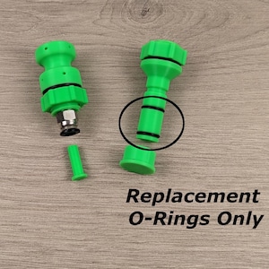 Puede incluir: Dos piezas de plástico verde con juntas tóricas negras. El texto "Replacement O-Rings Only" es visible debajo de las piezas.