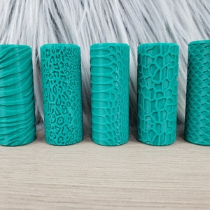 May include: Five teal-colored rubber rollers with different embossed patterns. The patterns include a wavy line, leopard print, snake skin, and two different scales.