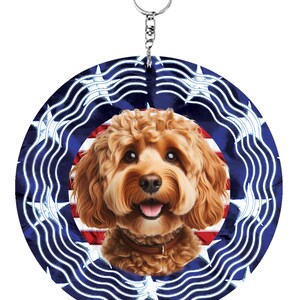 May include: A circular metal wind spinner featuring a portrait of a golden-brown curly-haired dog with a brown collar. The background displays a stylised American flag pattern with blue, white, and red colours, including white stars and stripes.