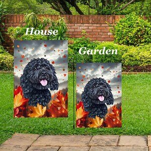 May include: Two garden flags featuring a black dog with a pink tongue, surrounded by autumn leaves. The flags are labeled "House" and "Garden" in white text, set against a backdrop of a cloudy sky and green foliage.