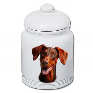 May include: White ceramic jar with a lid, featuring a detailed illustration of a Doberman Pinscher's face. The dog has brown fur and a happy expression. The jar has black stripes near the base.