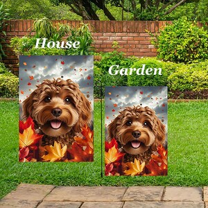 May include: Two garden flags featuring a smiling brown dog with autumn leaves. The flags are labeled "House" and "Garden" in white text. The background includes a cloudy sky, green grass, and a brick wall.