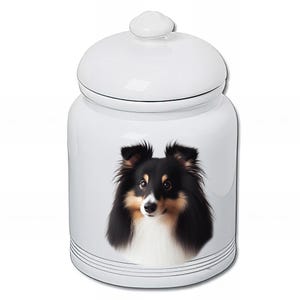 Peut inclure: Pot en céramique blanc avec couvercle, orné d'un portrait détaillé d'un chien Sheltie. Le chien a des poils noirs, bruns et blancs. Le pot a un design simple avec des rayures noires près de la base.