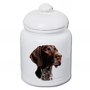May include: White ceramic jar with a lid, featuring a detailed portrait of a brown and white German Shorthaired Pointer. The jar has a glossy finish and is decorated with black horizontal lines near the base.