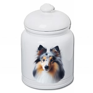Peut inclure: Un pot en céramique blanc avec un couvercle, orné d'un portrait détaillé d'un chien Shetland. Le chien a un mélange de fourrure noire, marron et blanche. Le pot a une finition brillante et est décoré de rayures noires près de la base.