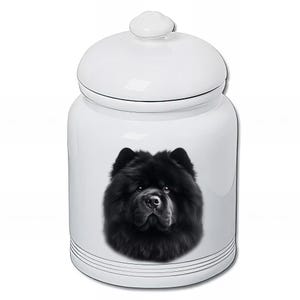 Puede incluir: Tarro de cerámica blanco con tapa, con una imagen detallada de la cara de un perro Chow Chow negro. El tarro tiene un acabado brillante y está decorado con finas líneas negras alrededor de la base.