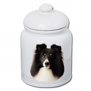 Peut inclure: Pot en céramique blanc avec couvercle, orné d'un portrait détaillé d'un chien Sheltie noir, blanc et marron. Le pot a une finition lisse avec une ligne noire décorative autour de la base.