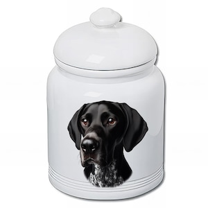 May include: White ceramic jar with a lid, featuring a black dog portrait. The dog has brown eyes and a black coat with white markings. The jar has a glossy finish and black stripes near the base.