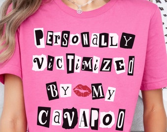 May include: Pink t-shirt with the text "PERSONALLY VICTIMIZED BY MY CAVAPOO" in black letters with a red lip print between "BY" and "MY".