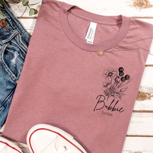 May include: A dusty rose t-shirt with a black floral design and the text "Bubbie Est 2024" printed on the front.