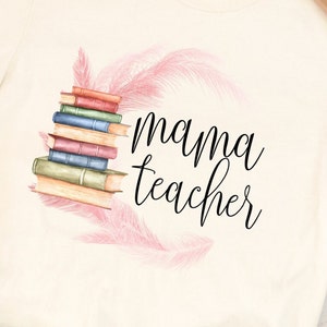 May include: A white t-shirt with a stack of books and pink feathers surrounding the text "mama teacher".