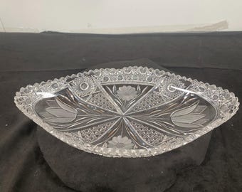 May include: A clear glass serving dish with a scalloped edge and intricate cut glass design. The dish features a floral pattern with tulips and daisies.
