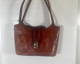 May include: A brown leather handbag with a decorative design and a gold clasp. The bag has two straps and is hanging from a hook.