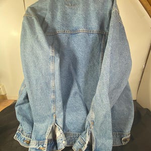 May include: A blue denim jacket with a button-up front and long sleeves. The jacket has a classic design with two pockets on the chest and two pockets on the hips.
