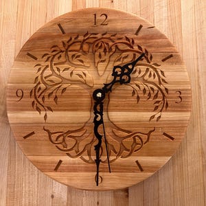 Puede incluir: Reloj de pared redondo de madera con un diseño de árbol de la vida tallado en la esfera. El reloj tiene manecillas e indicadores de hora negros. La esfera del reloj tiene aproximadamente 30 cm de diámetro.