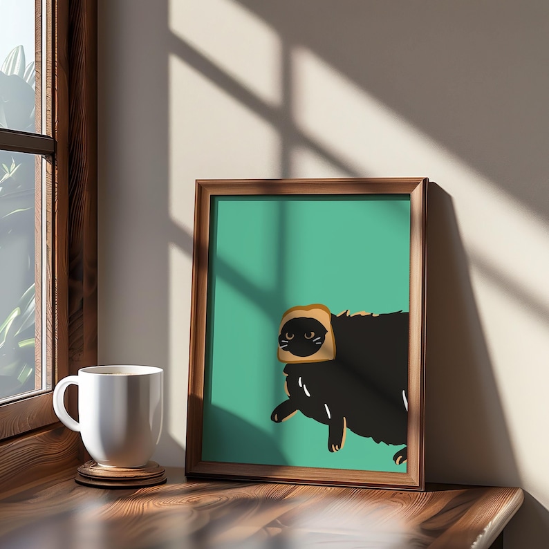 A framed illustration of a black cat wearing a slice of bread on its head. The cat is facing the left side of the image and is on a green background. The frame is brown wood.