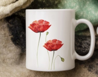 May include: White ceramic mug with a design of two red poppies on a white background. The mug is sitting on a brown and white fuzzy blanket.