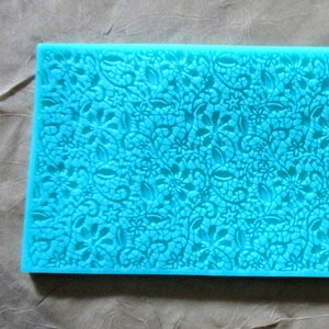 May include: A blue silicone baking mat with a lace pattern. The mat is designed for use with fondant or other edible decorations.