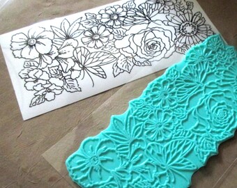 May include: A teal blue rubber stamp with a floral design. The stamp is on a clear plastic sheet.