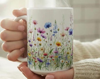 May include: White ceramic mug featuring a vibrant floral design with colorful wildflowers. The mug has a curved handle and is filled with a hot beverage, with steam rising from the top. The flowers include pink, blue, yellow, and purple blooms.
