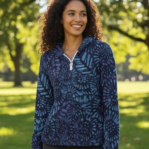 May include: A navy blue hooded sweatshirt with a blue and teal floral pattern. The sweatshirt has a white zipper and a hood. The model is smiling in a park setting.