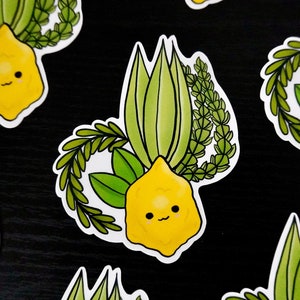 Puede incluir: Un conjunto de cuatro pegatinas coloridas que representan un limón con una cara sonriente y un manojo de hojas verdes. Las pegatinas son perfectas para añadir un toque de fantasía a tus pertenencias.