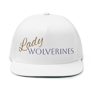 May include: A white flat-brimmed baseball cap with the words "Lady Wolverines" embroidered on the front in brown and navy blue. The cap has a green underside on the brim.