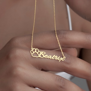 Può includere: Collana in oro con un ciondolo a forma di impronta di zampa e il nome "Beatrix" scritto in corsivo.
