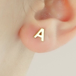 Peut inclure: Boucles d'oreilles en forme de lettre 'A' dorées. Les boucles d'oreilles sont petites et délicates, parfaites pour un usage quotidien.