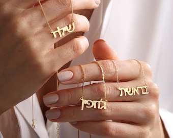 May include: Three gold necklaces with Hebrew lettering. The necklaces are layered and feature the names "דניאל", "שמואל", and "עטל".