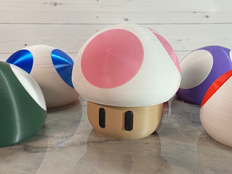 May include: A set of five 3D printed mushroom-shaped figurines. The figurines are painted in various colors, including green, blue, purple, pink, and white.