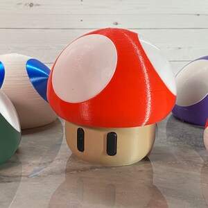 May include: A red and white mushroom-shaped toy with a beige base and two black dots. The mushroom is surrounded by other colorful mushroom-shaped toys.