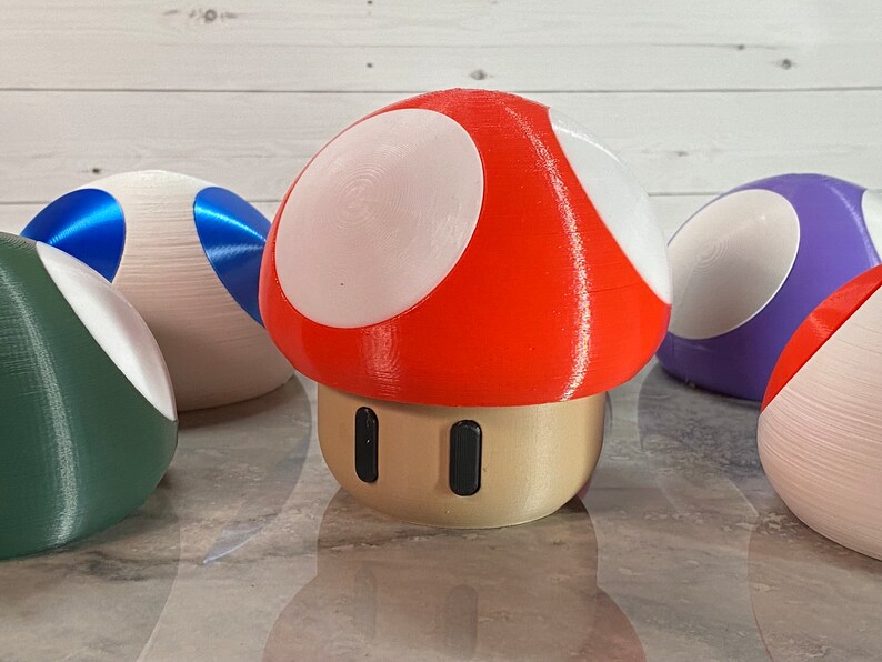 May include: A red and white mushroom-shaped toy with a beige base and two black dots. The mushroom is surrounded by other colorful mushroom-shaped toys.
