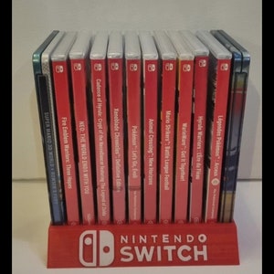 Peut inclure: Un support de jeu Nintendo Switch rouge avec le logo Nintendo Switch, contenant plusieurs boîtiers de jeux. Les boîtiers de jeux ont des dos rouges avec des titres de jeux comme "Animal Crossing" et "Mario Strikers".