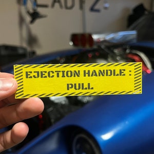 May include: A yellow and black striped sticker with the text "EJECTION HANDLE: PULL" in black letters.