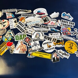 May include: A collection of colorful stickers with various humorous and quirky sayings. The stickers feature a variety of designs, including cars, trucks, and people. Some of the sayings include "Race Car Driver", "Forklift Certified", and "I Am Compensating For Something".