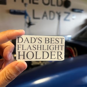 May include: White sticker with the text "Dad's Best Flashlight Holder" in black lettering.