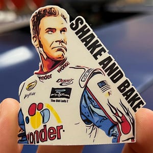 May include: A white sticker with a cartoon illustration of a race car driver wearing a blue and red racing suit. The driver is holding a steering wheel and the sticker says "Shake and Bake".